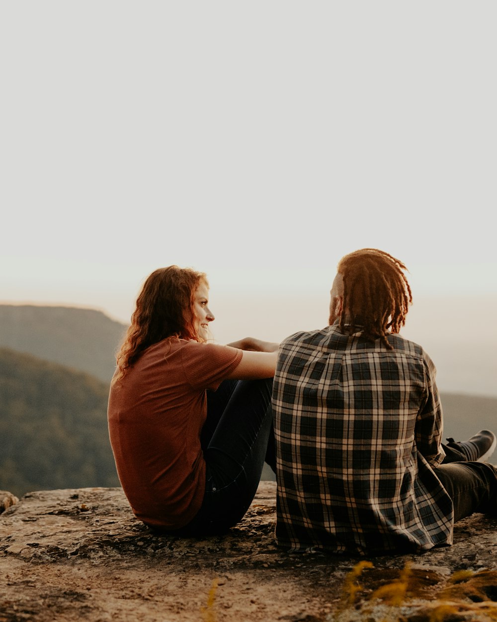 Two people sitting side by side on a rock, looking out over the hills together